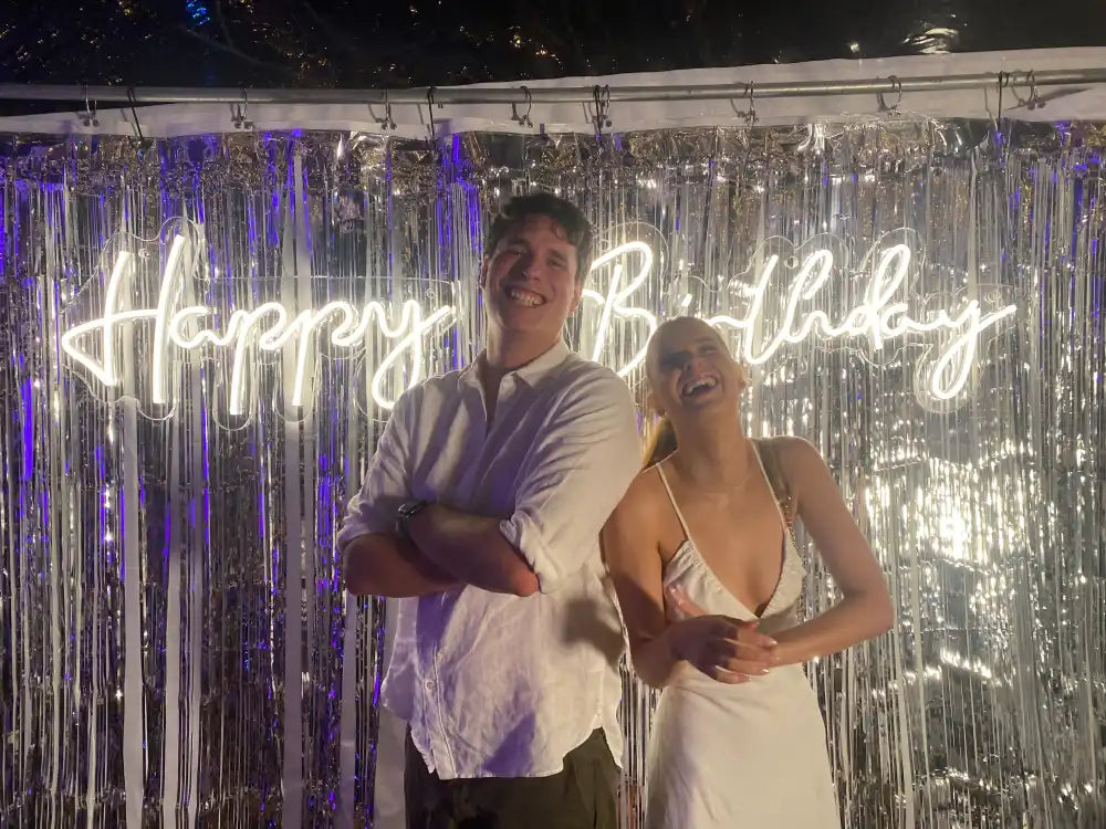 Two people in front of a ’Happy Birthday’ sign.